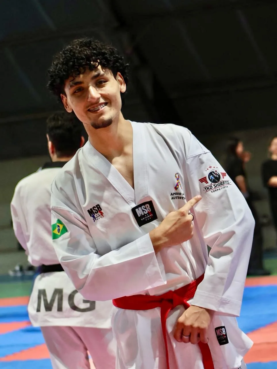 Atleta aponta para o emblema do TKD Shirato Competidor no dobok, em competição estadual