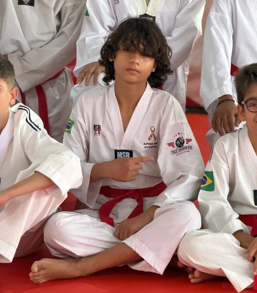Atletas sentados no tatame durante intervalo de treino, de dobok e faixa vermelha
