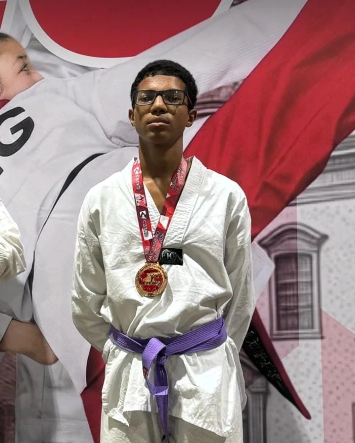Arthur Agripino no pódio com a medalha de ouro no peito, de dobok e faixa roxa