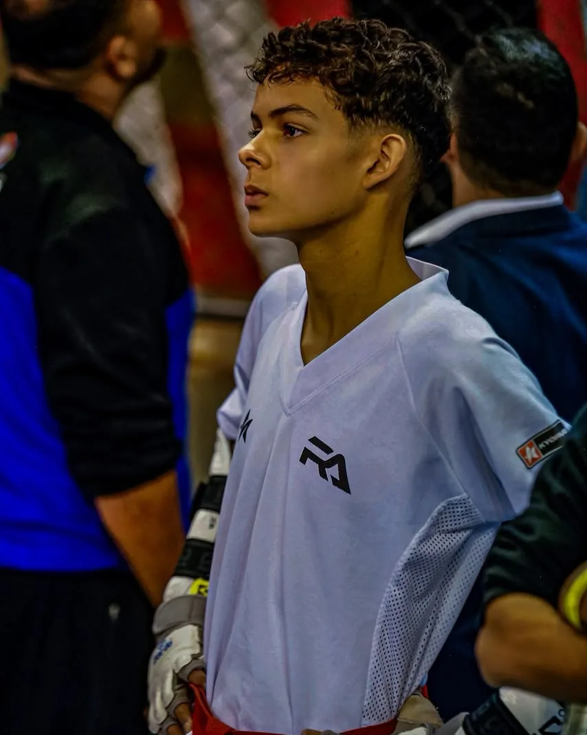 João Antônio Nazareth Santos perfilado antes da luta, de dobok branco e luvas de competição